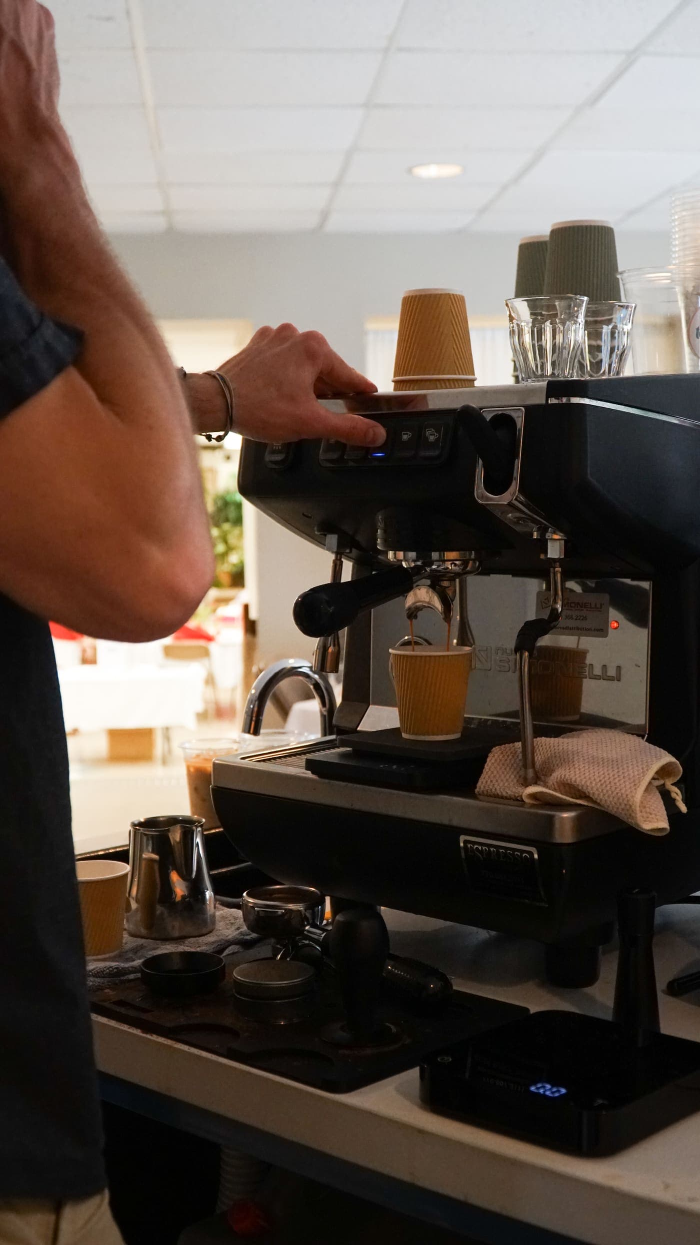 A barista working the espresso machine, warmed cups resting on top and shots extracting below