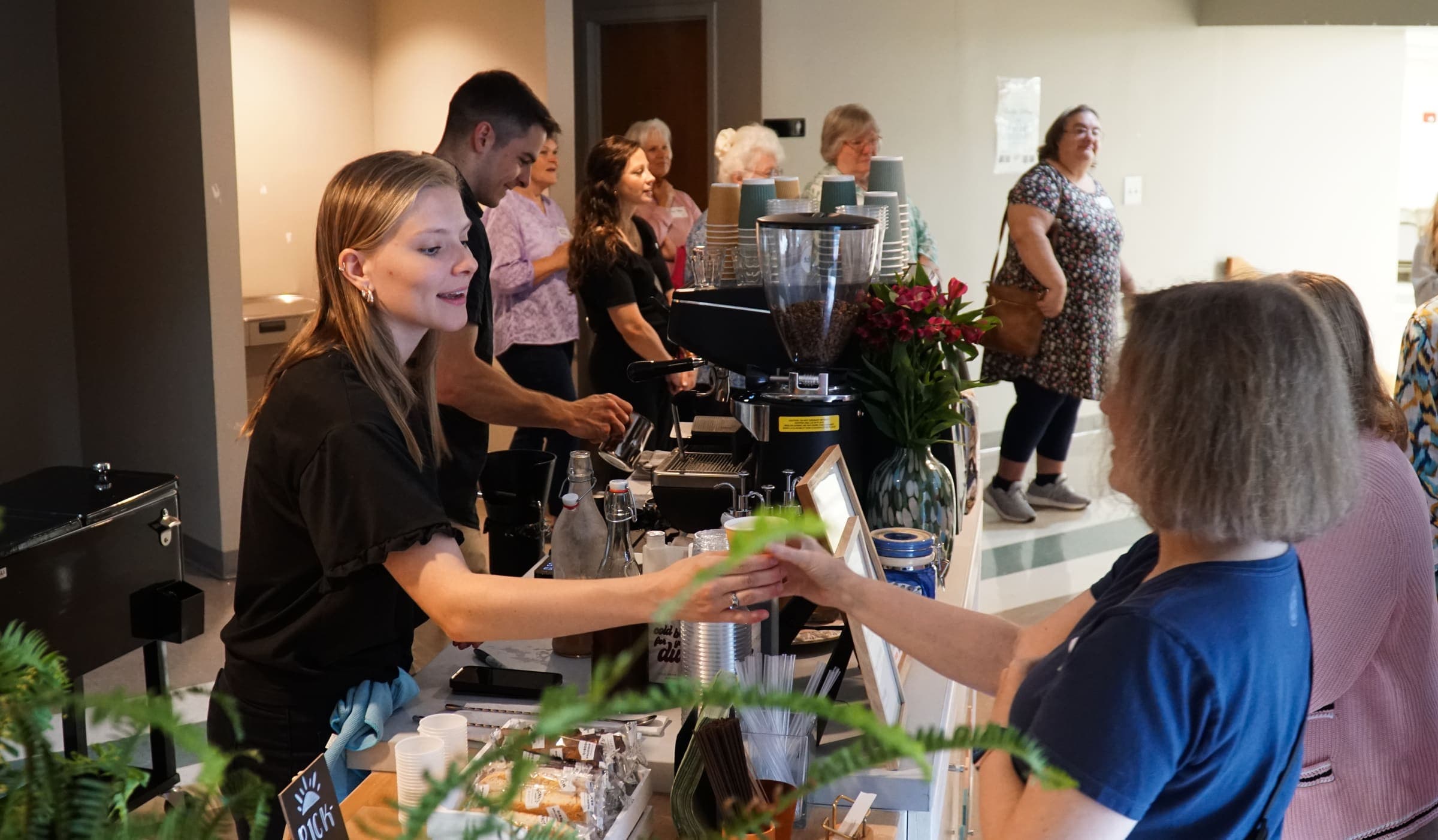 A barista hands an iced drink across the cart to a guest at an event