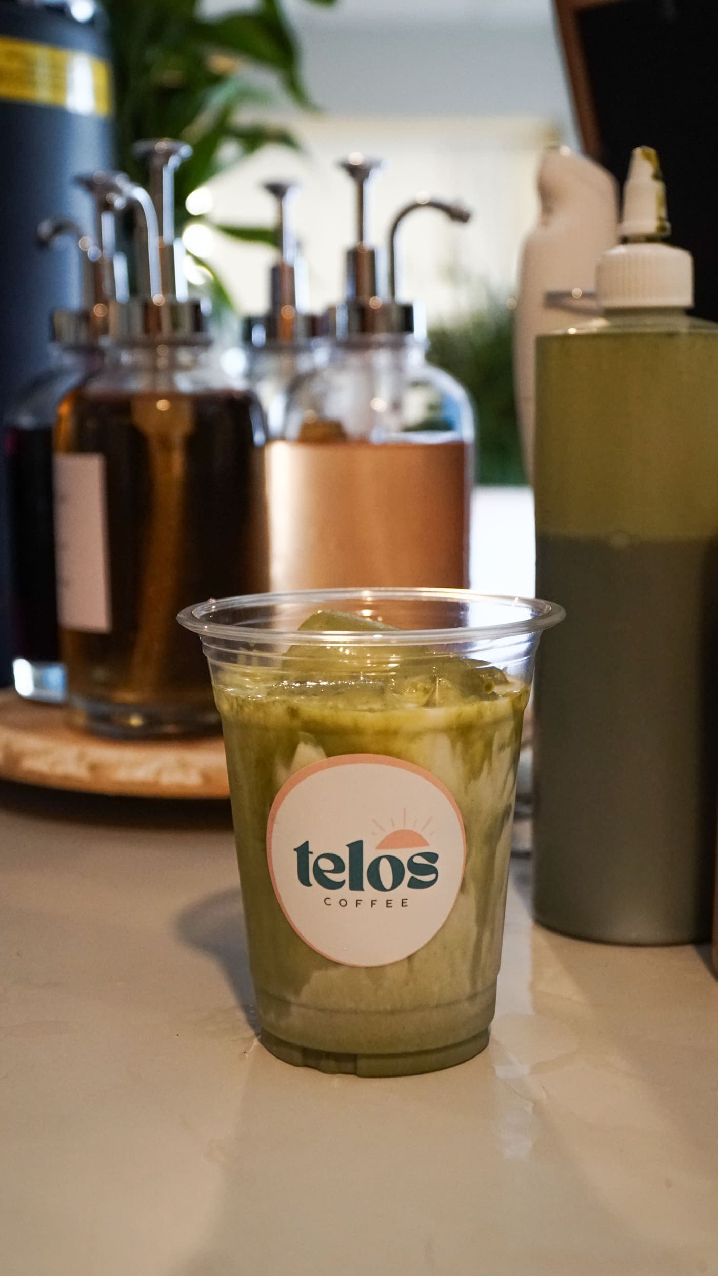 An iced matcha being finished in a branded Telos Coffee cup