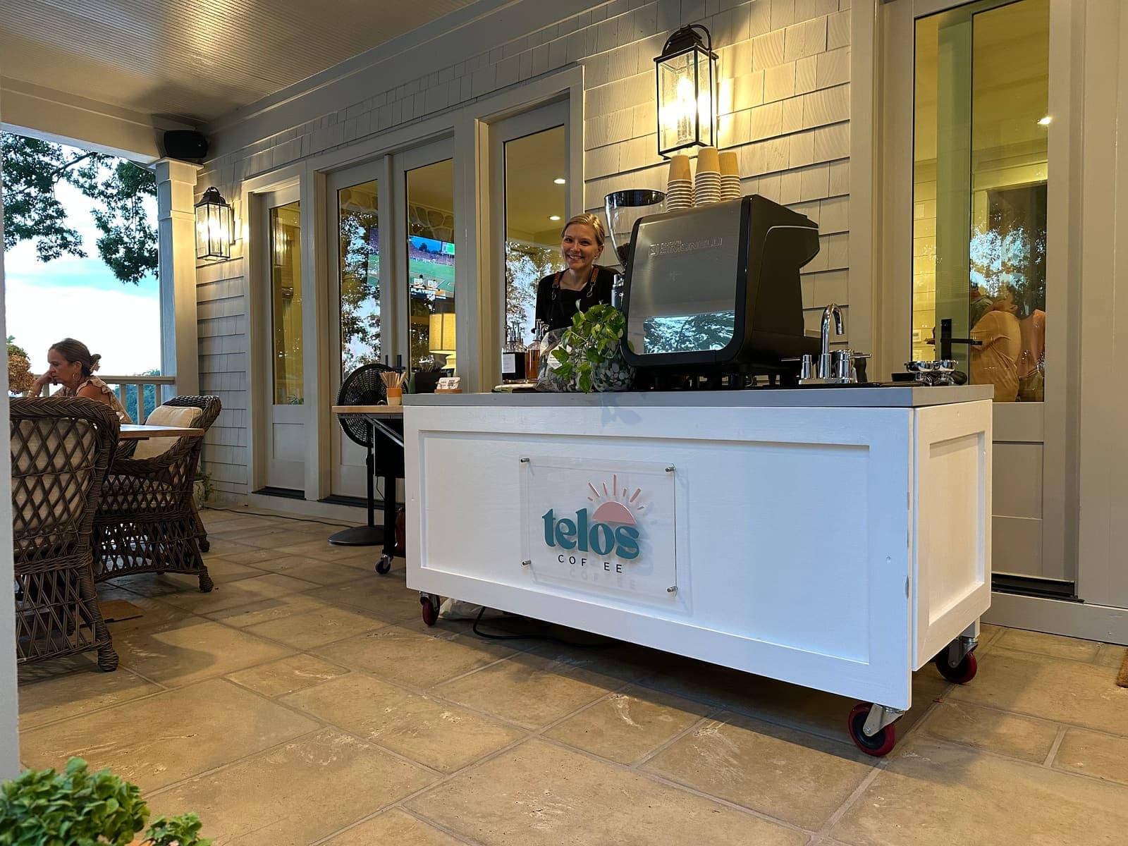 Melissa serving from the Telos Coffee cart on a covered porch, guests seated at a table nearby