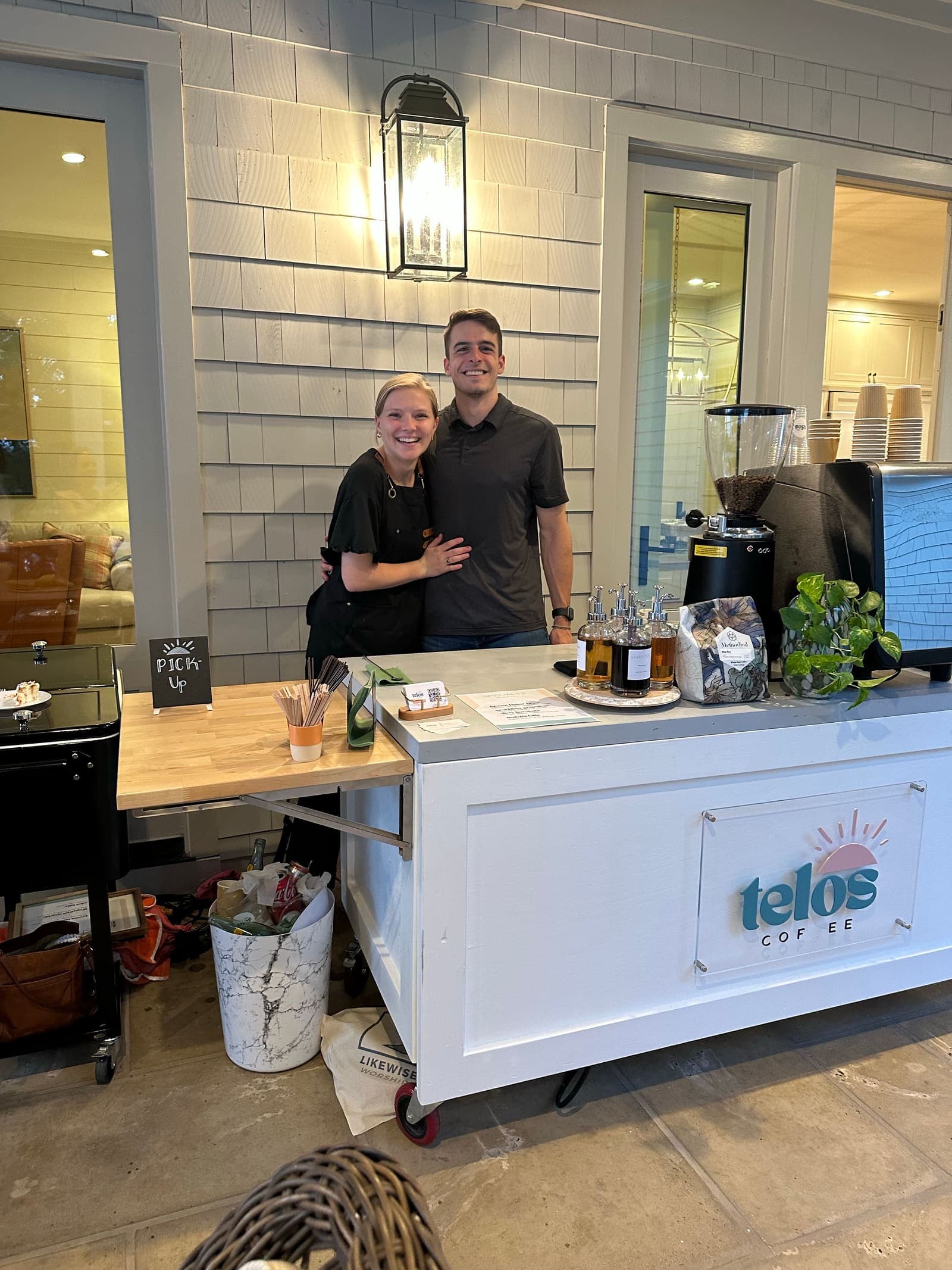 Tim and Melissa behind the Telos Coffee cart indoors, set up and ready to serve